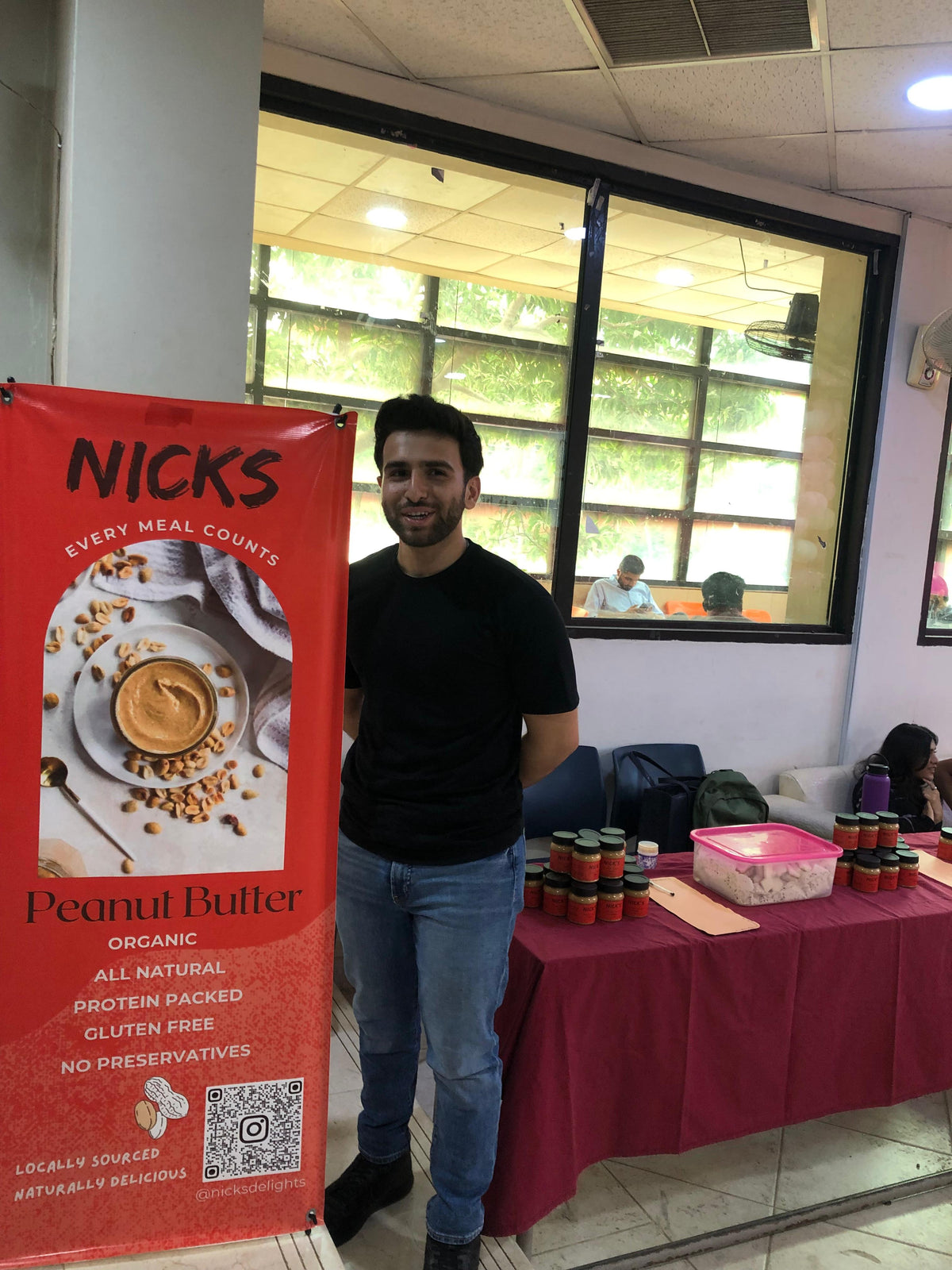 Aneeq standing beside the first NICK'S peanut butter stall at his university, with jars stacked on the table