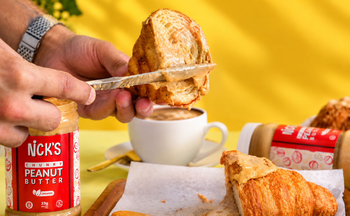 Close-up of a knife spreading NICK'S chunky peanut butter on a croissant