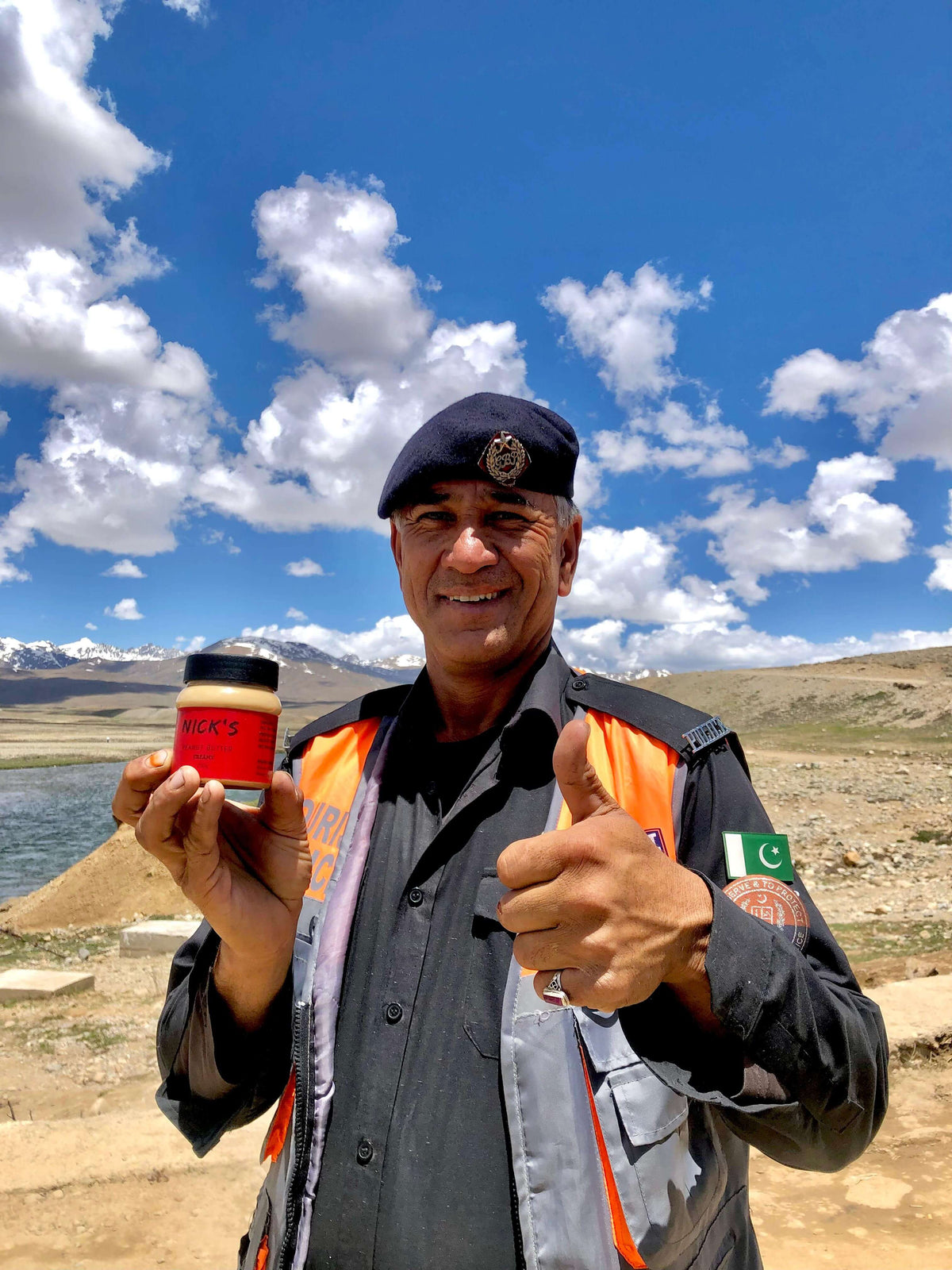 A smiling man in the northern mountains of Pakistan holding up a jar of NICK'S peanut butter and giving a thumbs up
